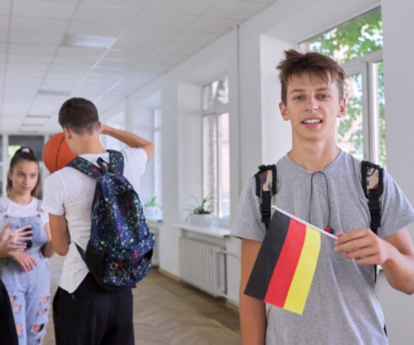 Student teenager male with the flag of Germany inside school, school children group background. Europe, Germany, education and youth, patriotism, people concept